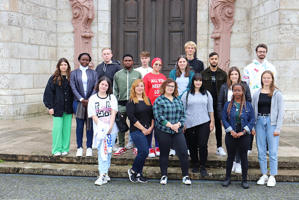 Eine Gruppe junger Menschen steht auf den Stufen des Münsters und schaut freundlich in die Kamera. 