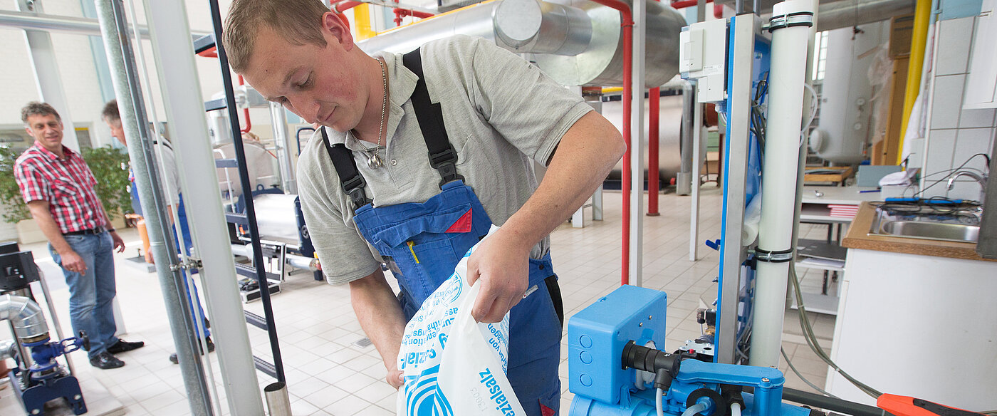 Ein junger Auszubildender im Blaumann schüttet Spezialsalz in eine Maschine.