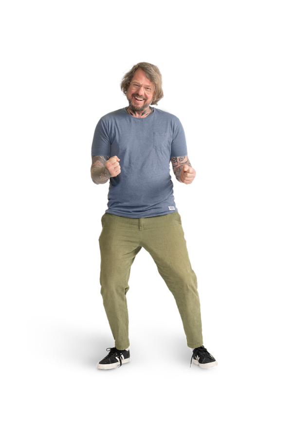 Ein Mann mit Brille, hellblauem Shirt, tätowierten  Armen und khakifarbener Hose.  
