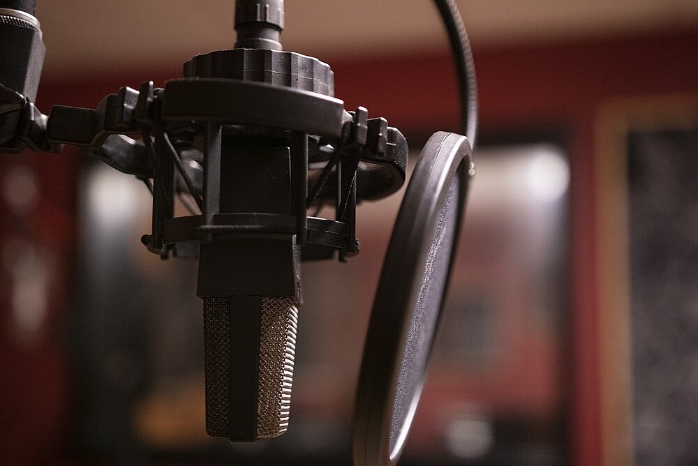 Man sieh ein Mikrofon und einen Kopfhörer und im Hintergrund ein Studio.