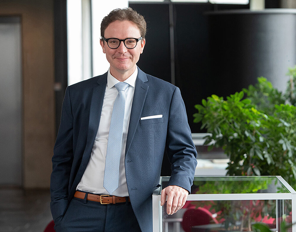 Ein freundlich aussehender Mann im mittleren Alter mit Brille im blauen Anzug.