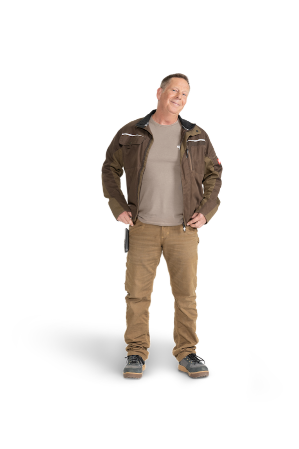 Ein Mann mit olivfarbener Arbeitsjacke, Cargo-Hose und grauem T-Shirt.