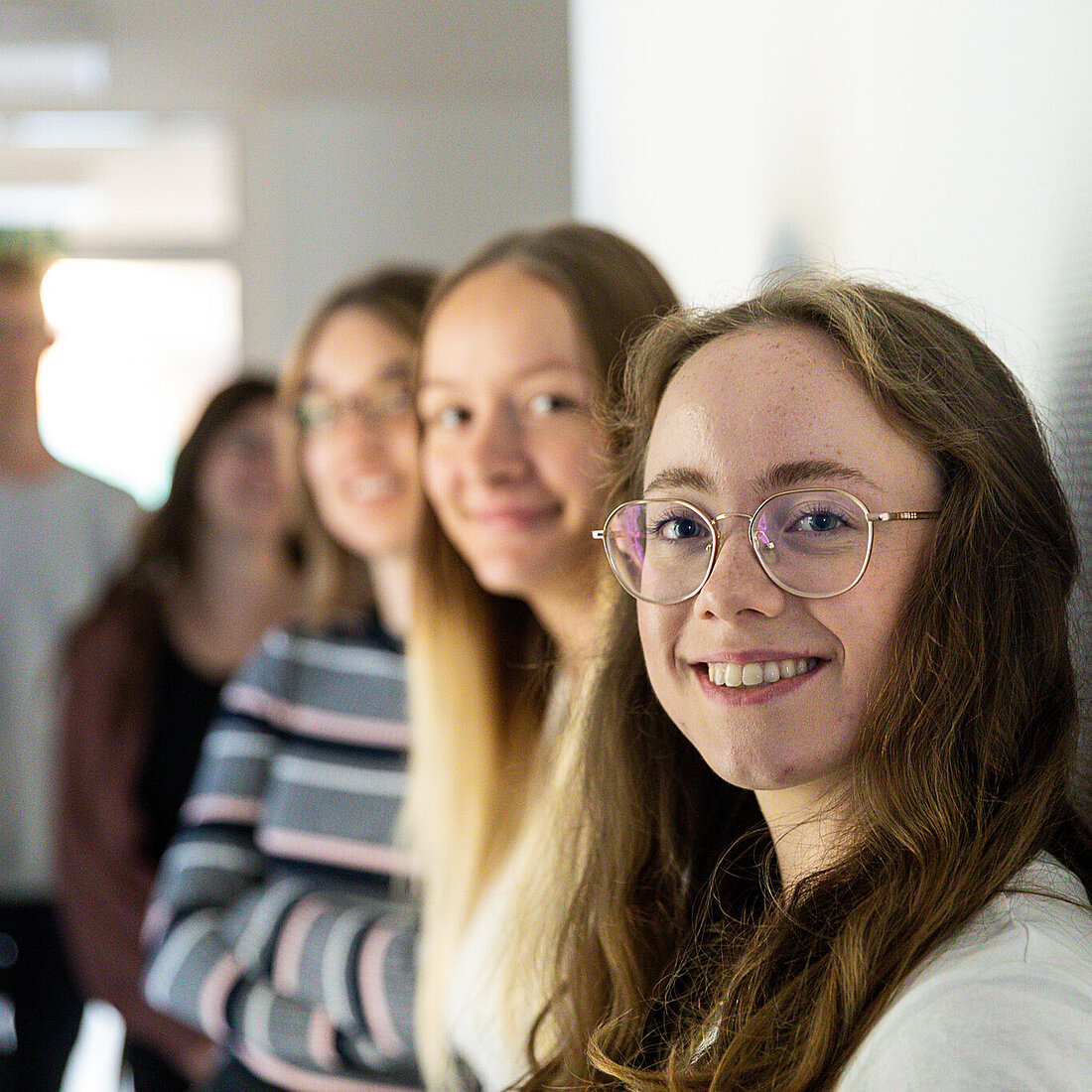 Eine Gruppe junger Frauen steht an eine Wand gelehnt, alle schauen lächelnd in die Kamera.