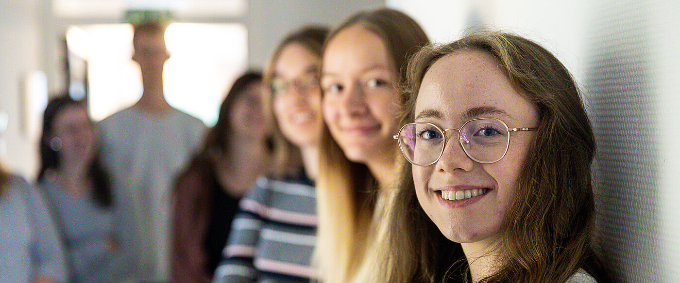 Eine Gruppe junger Frauen steht an eine Wand gelehnt, alle schauen lächelnd in die Kamera.