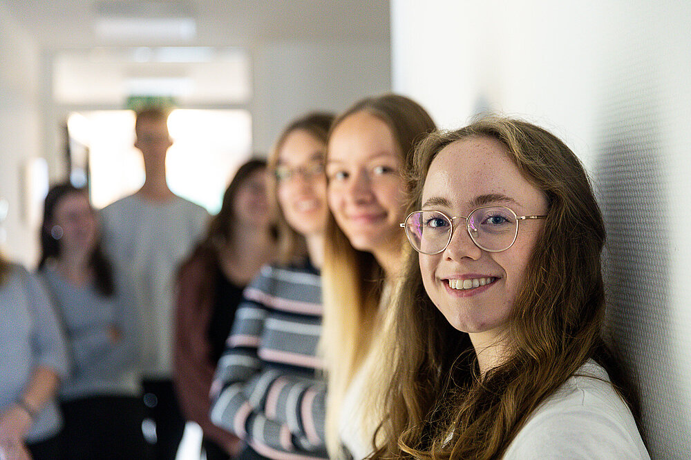 Eine Gruppe junger Frauen steht an eine Wand gelehnt, alle schauen lächelnd in die Kamera.