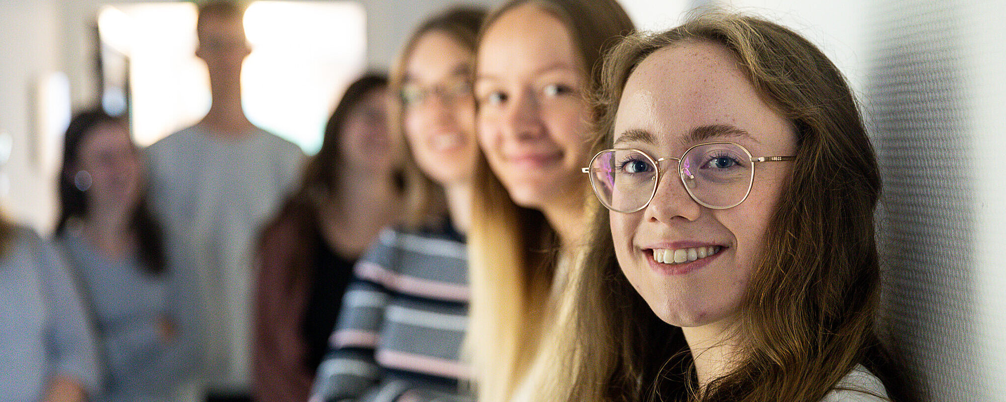 Eine Gruppe junger Frauen steht an eine Wand gelehnt, alle schauen lächelnd in die Kamera.