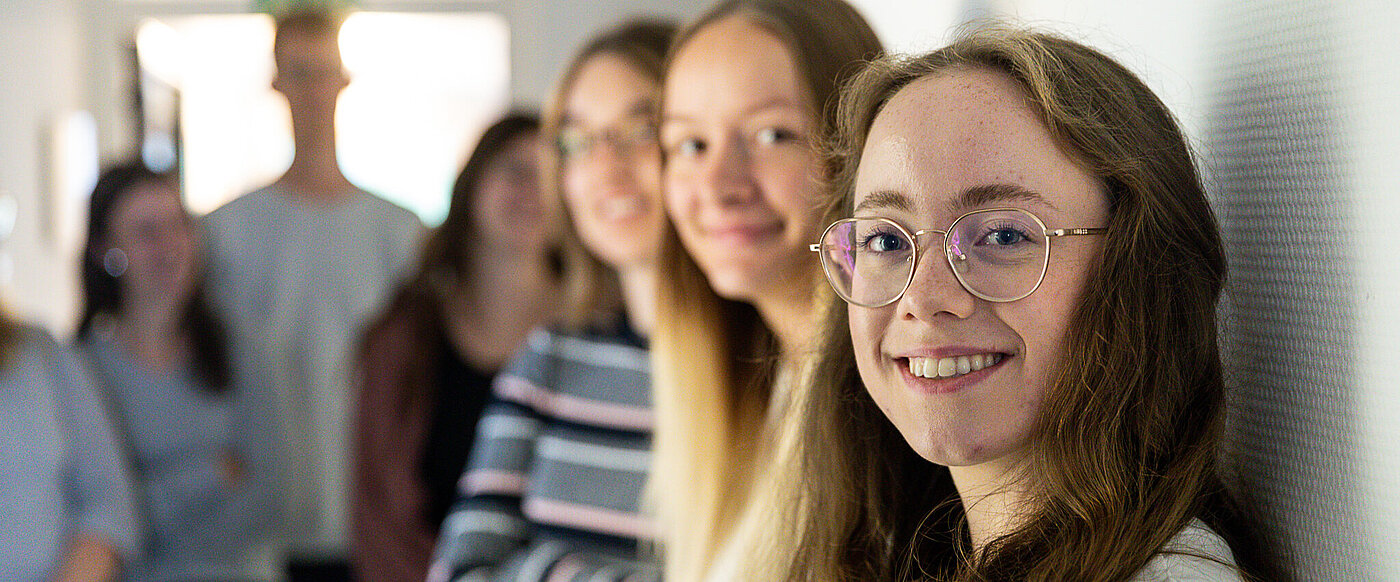 Eine Gruppe junger Frauen steht an eine Wand gelehnt, alle schauen lächelnd in die Kamera.