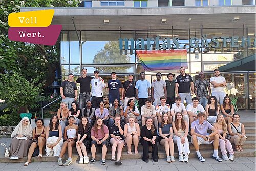 Eine diverse Gruppe junger Menschen sitzt auf einer Treppe vor einer Unterkunft in Berlin.