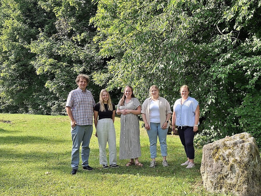 Ein großer Mann und vier Frauen stehen nebeneinander auf einer grünen Wiese.