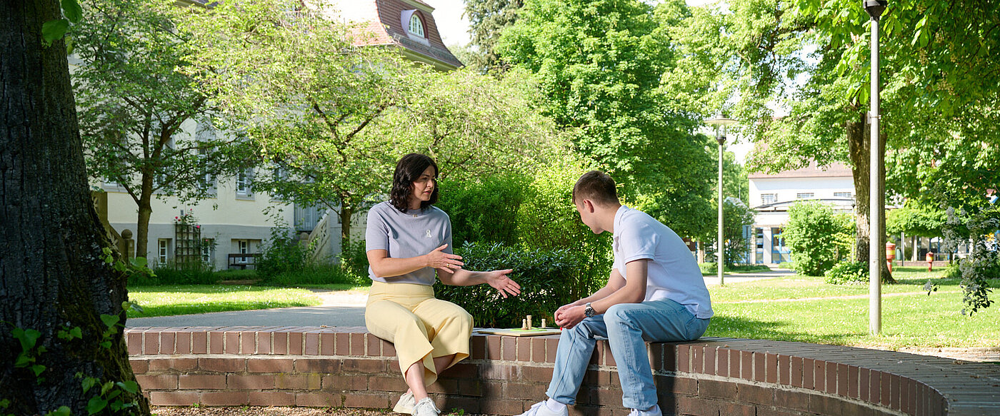 Eine junge Frau und ein Mann im mittleren Alter stehen vor einem großen Baum.