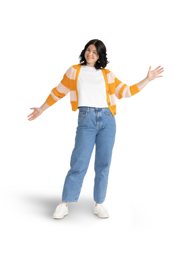 Eine Frau mit mittellangen, dunklen Haaren, einer Jeans und einer gestreiften Strickjacke über einem weißen Shirt. 