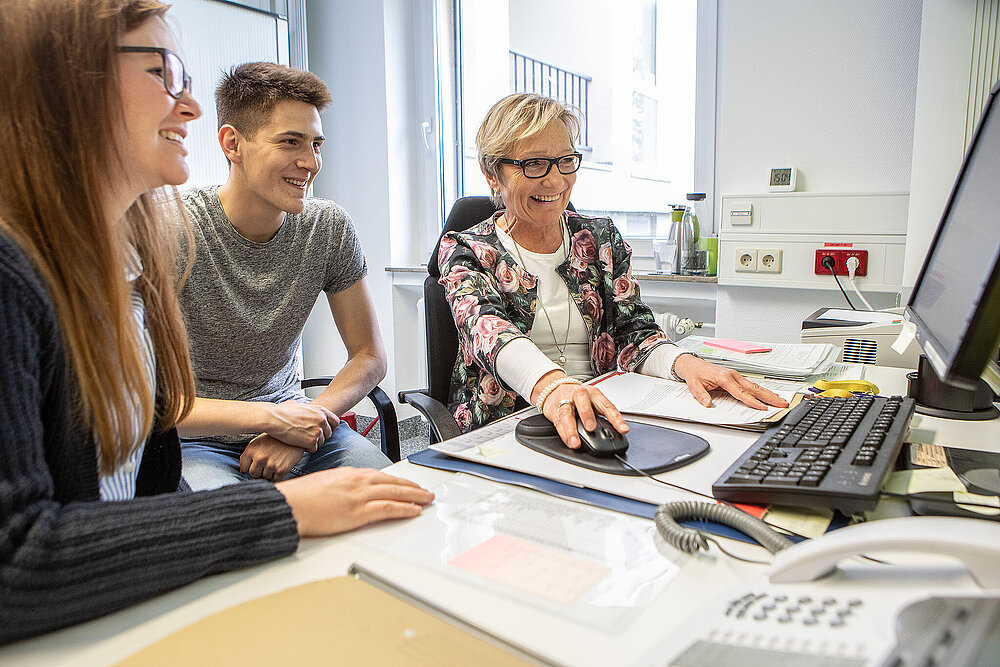 Zwei Männer und zwei Frauen sitzen an einem Tisch und blicken konzentriert auf einen gemeinsamen Bildschirm.