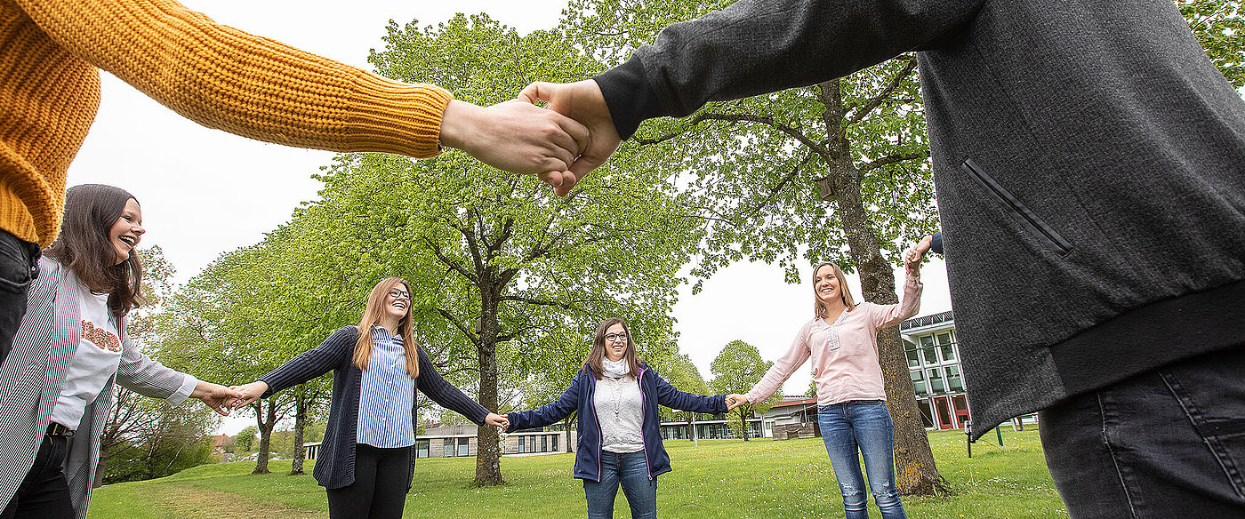 Eine Gruppe Azubis steht im Kreis und hält sich lachend an den Händen.