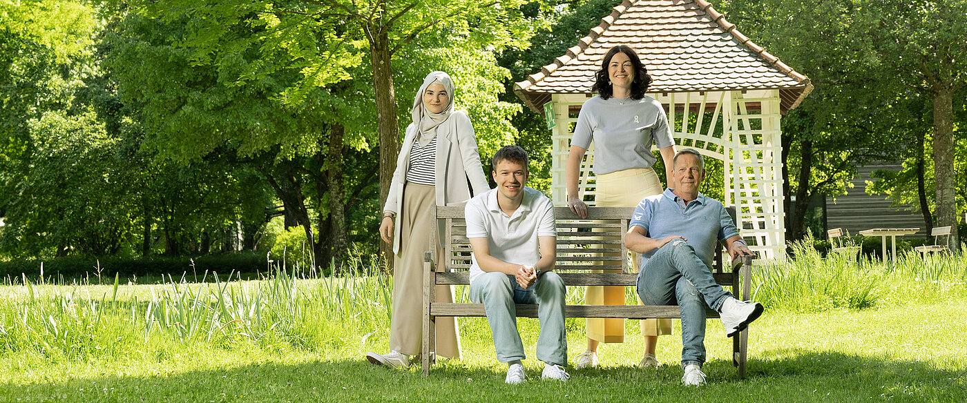 Vier Personen posieren auf einer Parkbank im Grünen.