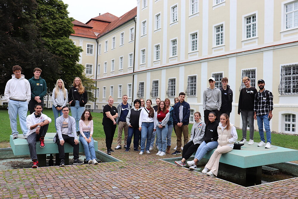 Eine große Gruppe junger Leute steht und sitzt vor einem Klostergebäude.