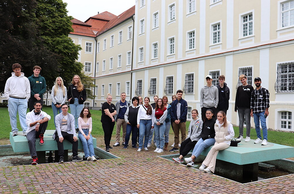 Eine Gruppe junger Frauen und Männer haben sich in zwei Reihen im Freien für ein Gruppenfoto aufgestellt.