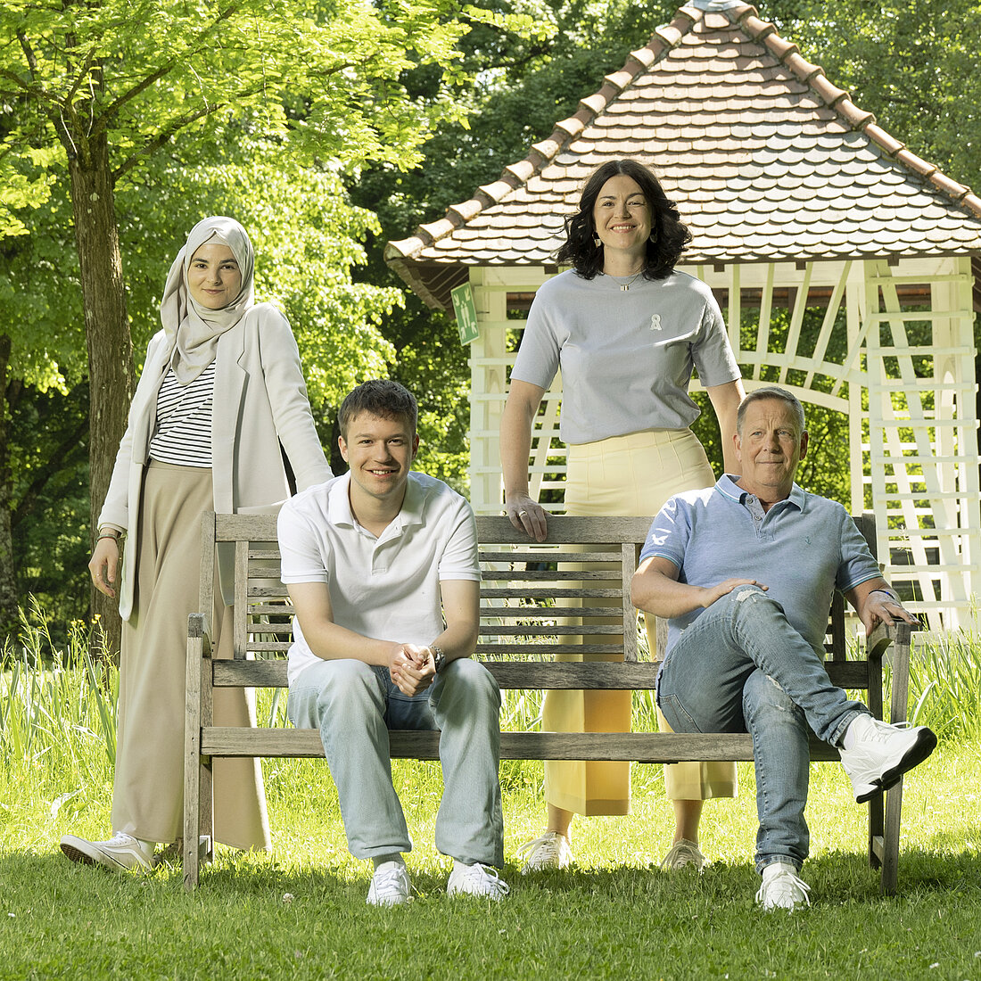 Vier Personen posieren auf einer Parkbank im Grünen.