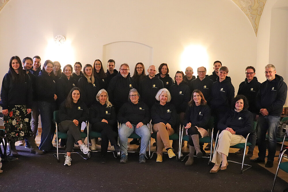 Eine Gruppe von rund 40 Personen sitzt und steht vor einer weißen Wand, alle tragen schwarze Hoodies mit ZfP-Logo.