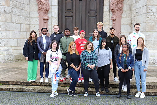 Eine Gruppe junger Menschen steht auf den Stufen des Münsters und schaut freundlich in die Kamera. 